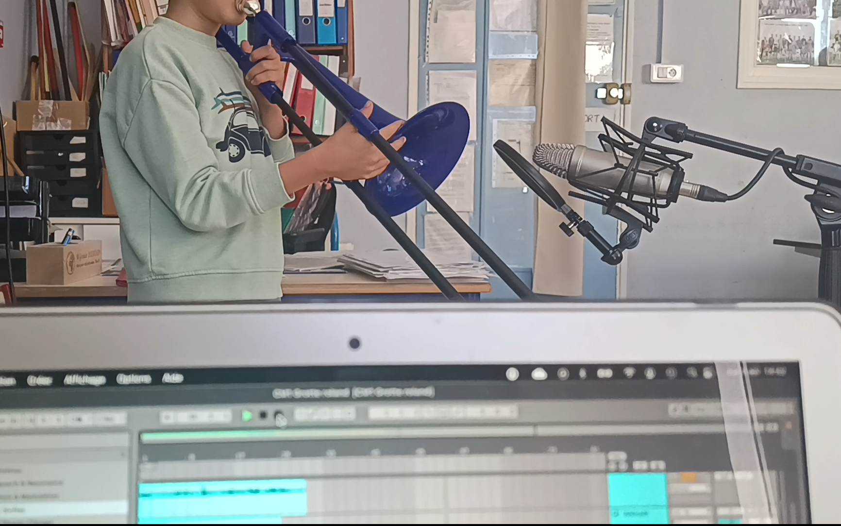 Un enfant joue du trombone, enregistré avec un micro et un logiciel de musique